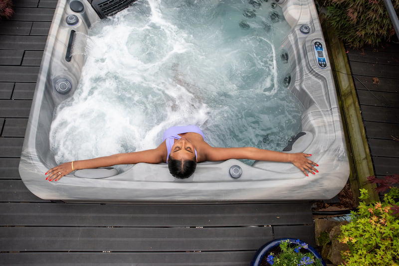 Woman relaxing in hot tub, with her arms stretched wide, resting on the side of the tub. The jets are turned on.