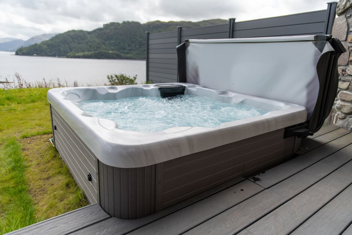 A Platinum Spas hot tub at a holiday let in Scotland. The hot tub is located next to some decking and next to a large lake.