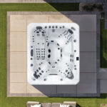 Overhead view of a Platinum Spas Maximus hot tub on a paved patio bordered by lawn, showing seats and jets