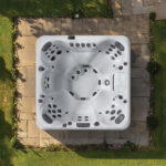 Overhead view of a Platinum Spas Sicily hot tub on a paved garden patio, showing six jetted seats and control panel